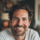 Homme souriant avec barbe, fond flou.