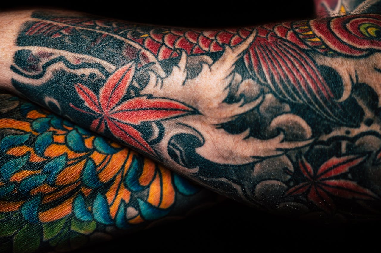 Detailed close-up of colorful sleeve tattoos featuring floral and abstract designs, showcasing artistic creativity.