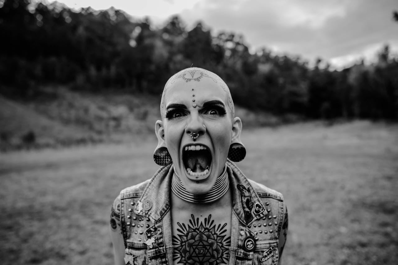 Monochrome portrait of a tattooed woman screaming in a natural setting, showcasing bold self-expression.